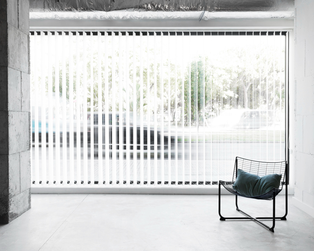 White blinds in the living room with a modern chair overlooking to the outside garden