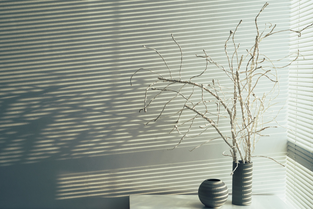Blinds setting the mood for the room. Vase with a dried plant on the table with wabi-sabi style interior design