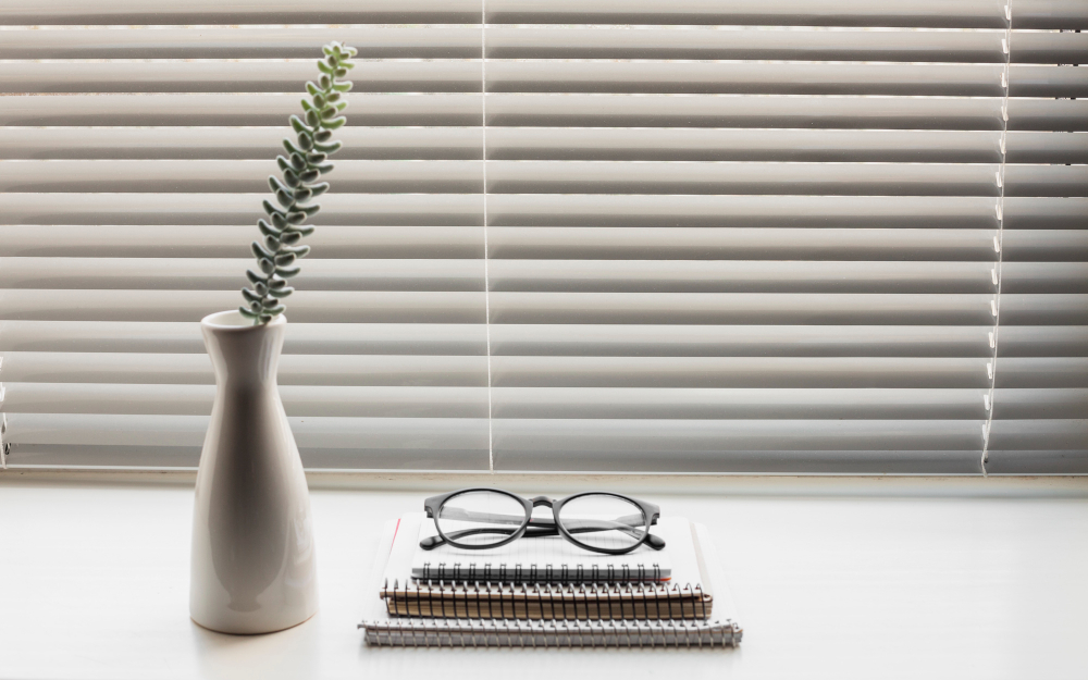 blinds illuminating light from the outside on an office desk with books, glasses and a succulent